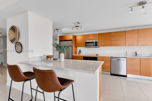 kitchen with light tile patterned floors, a peninsula, a sink, light countertops, and appliances with stainless steel finishes