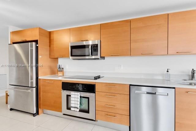 kitchen with a sink, light tile patterned floors, stainless steel appliances, and light countertops