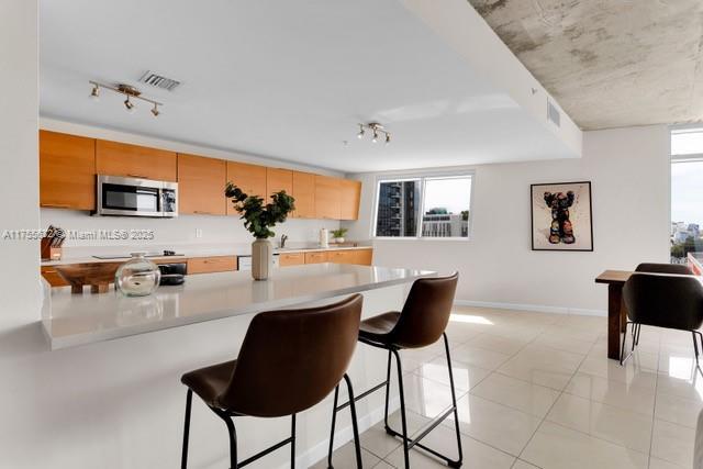 kitchen featuring visible vents, light countertops, stainless steel microwave, a kitchen bar, and track lighting