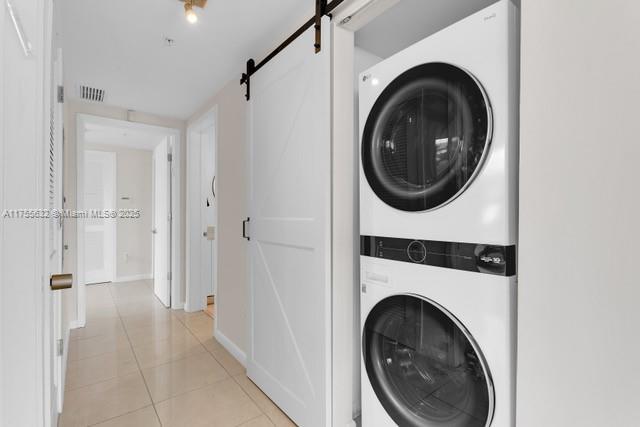 laundry room featuring light tile patterned floors, visible vents, a barn door, stacked washing maching and dryer, and laundry area