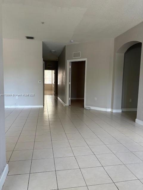 unfurnished room with arched walkways, visible vents, baseboards, and light tile patterned floors