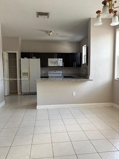 2111 Shoma Dr Unit 2111, Royal Palm Beach, FL 33414 - kitchen with white appliances, dark cabinetry, light stone countertops, light tile patterned floors, and a peninsula