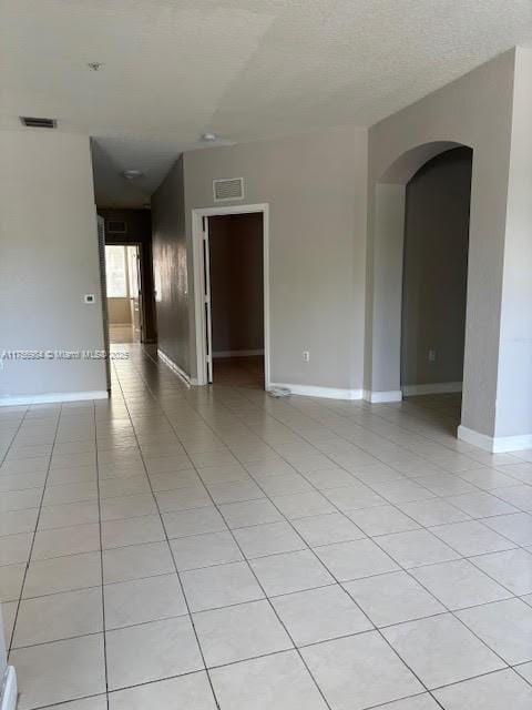 spare room with arched walkways, baseboards, visible vents, and light tile patterned floors