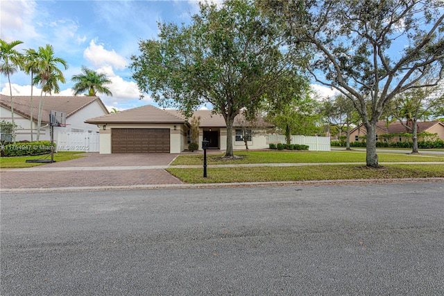 view of front facade with a tile roof, an attached garage, fence, decorative driveway, and a front lawn