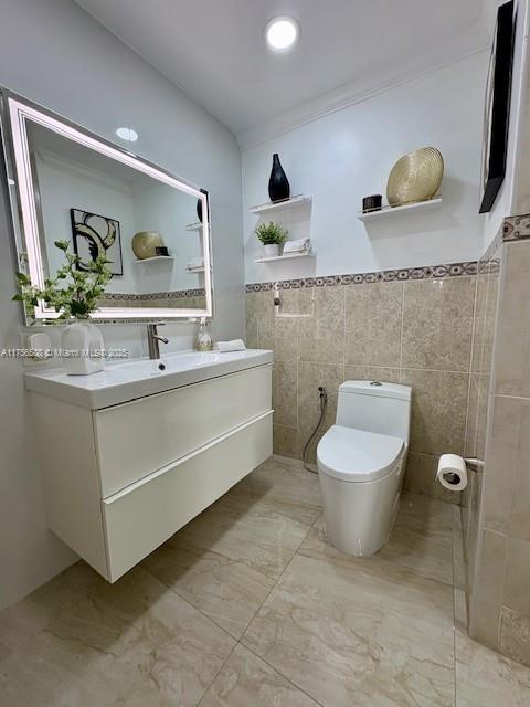 bathroom with marble finish floor, vanity, toilet, and tile walls