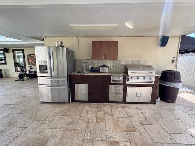 kitchen with stone tile floors, a sink, stainless steel fridge with ice dispenser, light countertops, and decorative backsplash