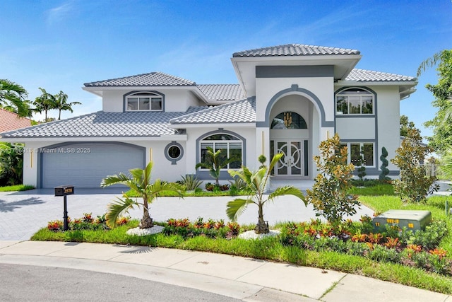 mediterranean / spanish-style house with a garage, decorative driveway, a tile roof, and stucco siding