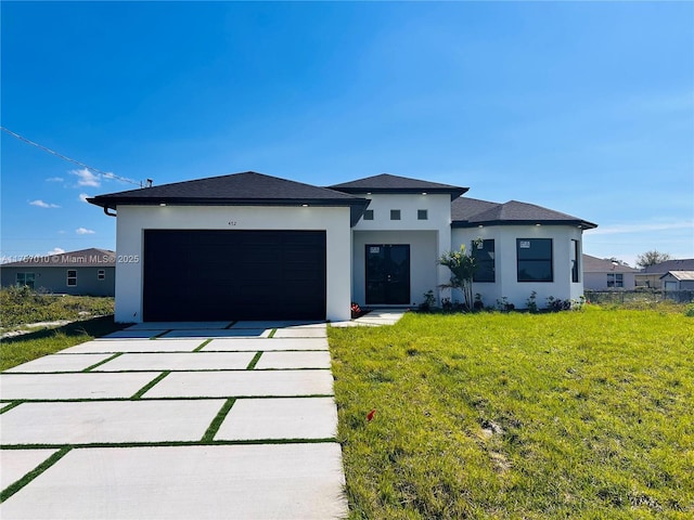 prairie-style house featuring a front lawn, concrete driveway, an attached garage, and stucco siding