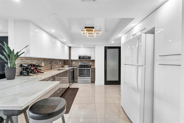 kitchen with light stone counters, white cabinets, appliances with stainless steel finishes, backsplash, and modern cabinets