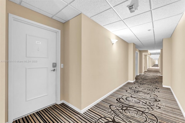 hallway with a paneled ceiling, baseboards, and visible vents