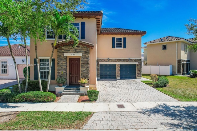 mediterranean / spanish home featuring decorative driveway, stucco siding, an attached garage, fence, and stone siding