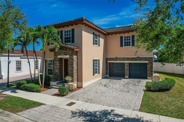 mediterranean / spanish-style house with an attached garage, fence, stone siding, decorative driveway, and stucco siding