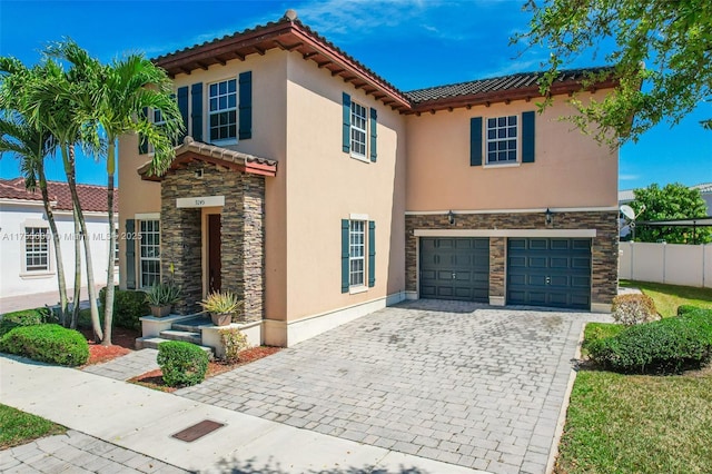 mediterranean / spanish-style home featuring stone siding, fence, decorative driveway, and stucco siding