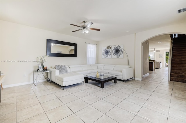 living room with light tile patterned floors, visible vents, arched walkways, ceiling fan, and stairs