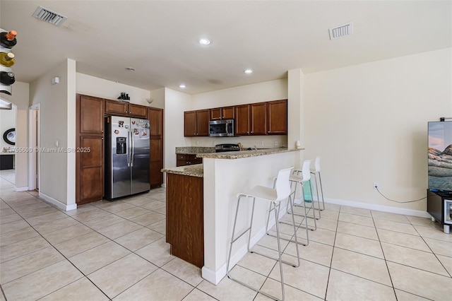 kitchen featuring light tile patterned floors, appliances with stainless steel finishes, a breakfast bar area, and visible vents