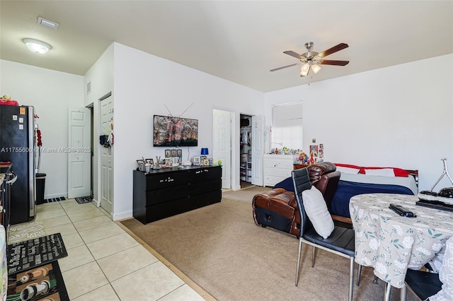 interior space featuring a ceiling fan, freestanding refrigerator, light carpet, and light tile patterned floors