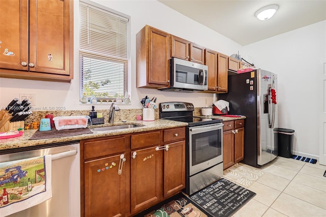 kitchen with light tile patterned floors, light stone counters, brown cabinets, stainless steel appliances, and a sink