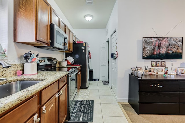 kitchen with light tile patterned floors, stainless steel appliances, brown cabinetry, and a sink