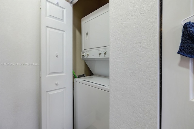 clothes washing area featuring a textured wall, laundry area, and stacked washer / drying machine