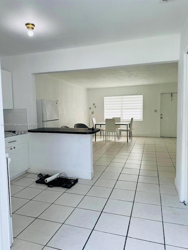 kitchen featuring dark countertops, light tile patterned flooring, backsplash, and freestanding refrigerator