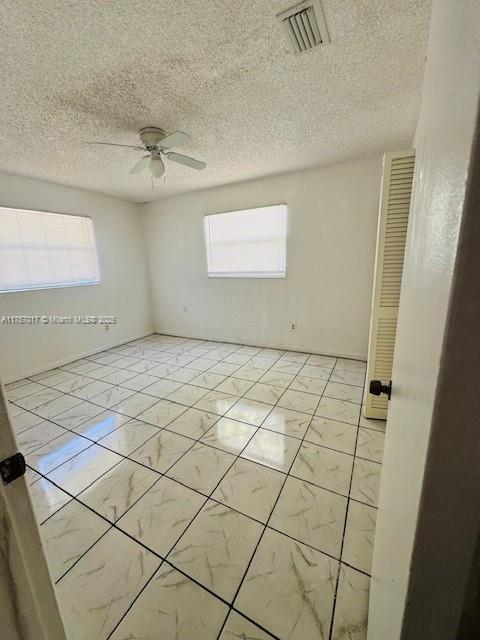 spare room with marble finish floor, ceiling fan, and visible vents