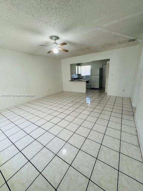 unfurnished living room featuring ceiling fan, a textured ceiling, and light tile patterned floors