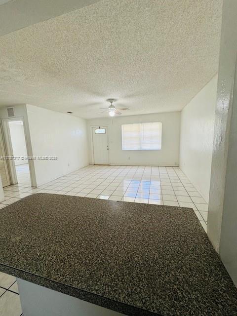 empty room featuring a textured ceiling, light tile patterned flooring, and a ceiling fan