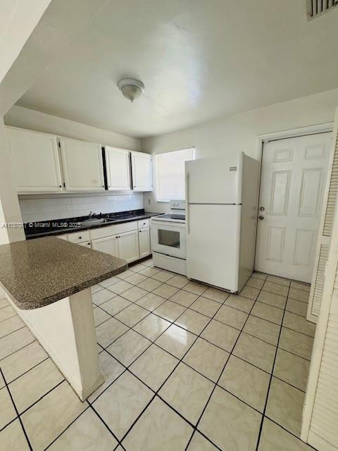 kitchen with white appliances, light tile patterned floors, visible vents, dark countertops, and white cabinetry