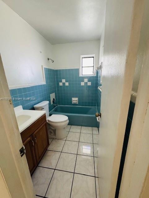 bathroom with toilet, shower / bathtub combination, tile patterned flooring, vanity, and tile walls