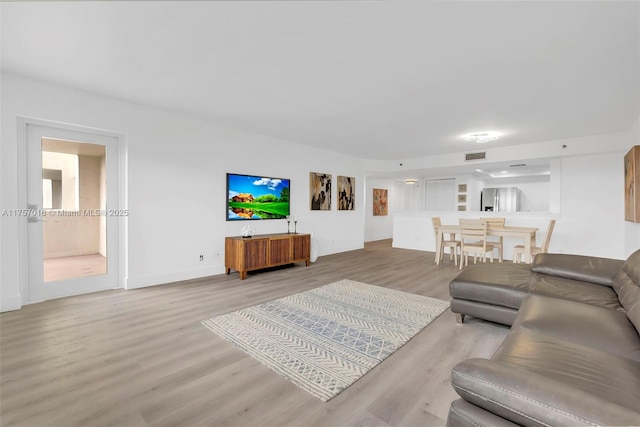 living room with light wood-type flooring, baseboards, and visible vents