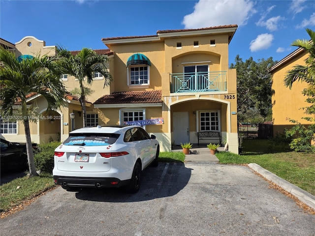 mediterranean / spanish-style home with a tile roof, fence, a balcony, and stucco siding