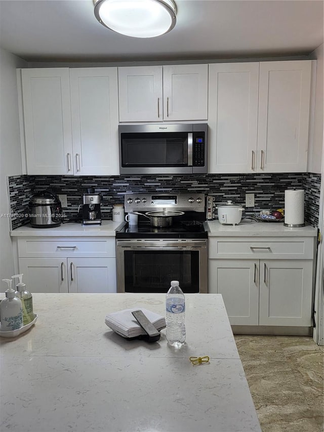 kitchen featuring appliances with stainless steel finishes, backsplash, light stone countertops, and white cabinets