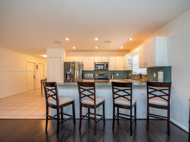 kitchen featuring a breakfast bar area, appliances with stainless steel finishes, white cabinets, a sink, and a peninsula