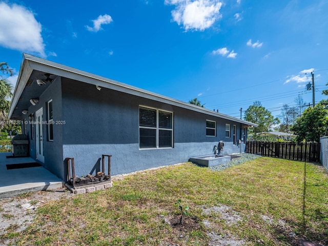 back of property featuring stucco siding, fence, and a yard