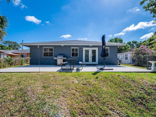 rear view of property featuring french doors, a yard, stucco siding, a patio area, and fence