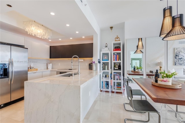 kitchen featuring light stone counters, a sink, modern cabinets, stainless steel fridge, and a peninsula