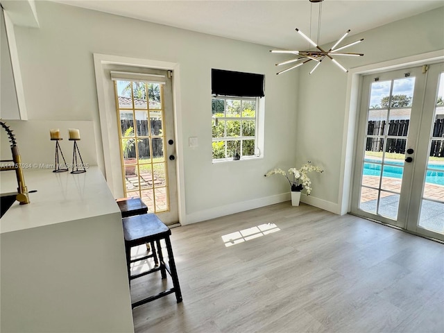 doorway with french doors, an inviting chandelier, light wood-style flooring, and baseboards