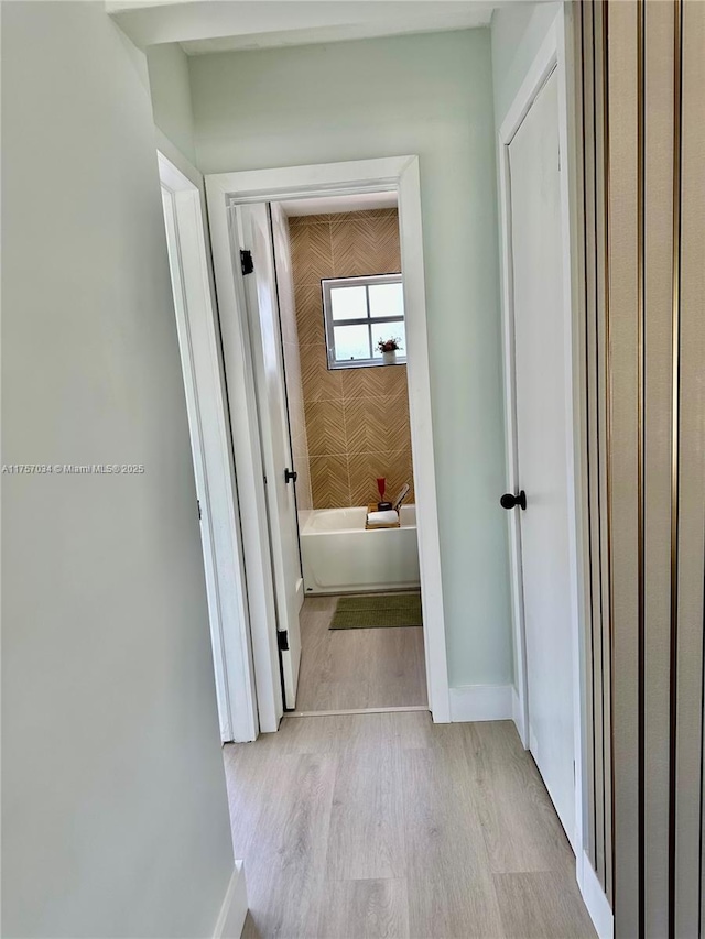 corridor featuring light wood-style flooring and baseboards