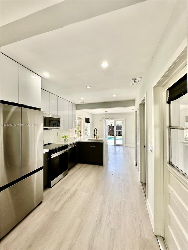 kitchen with a peninsula, visible vents, light wood-style floors, appliances with stainless steel finishes, and modern cabinets