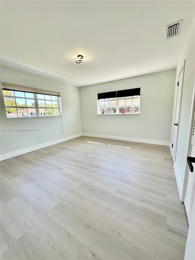 unfurnished room featuring light wood finished floors, plenty of natural light, visible vents, and baseboards