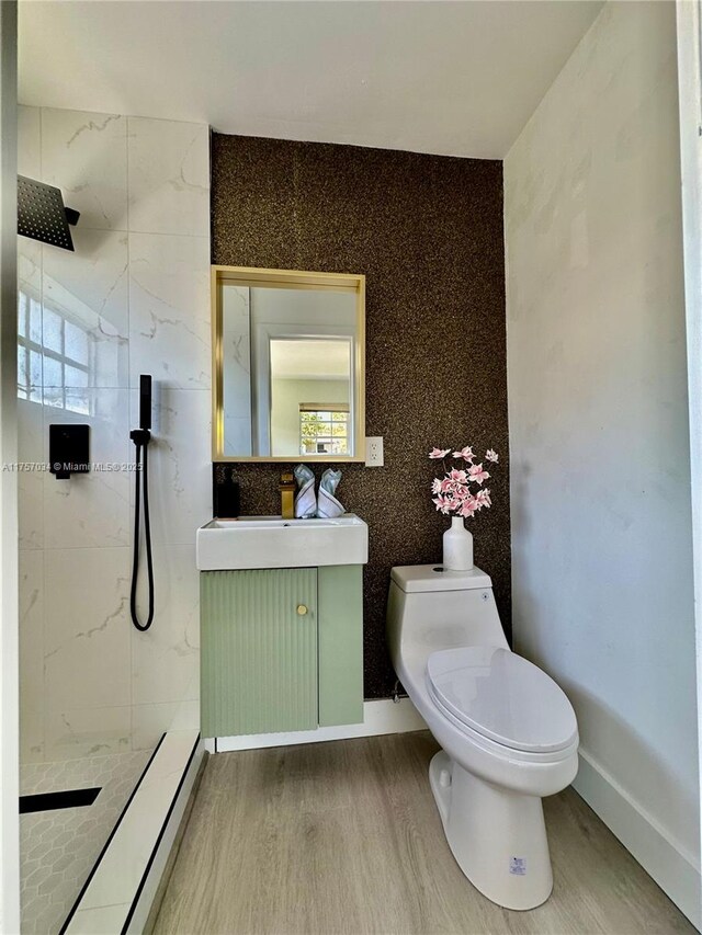 bathroom featuring a walk in shower, toilet, wood finished floors, vanity, and baseboards