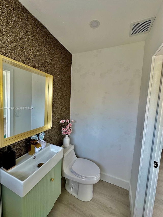 bathroom featuring toilet, wood finished floors, vanity, visible vents, and baseboards