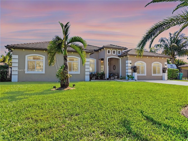 mediterranean / spanish home featuring a tiled roof, a front lawn, concrete driveway, and stucco siding