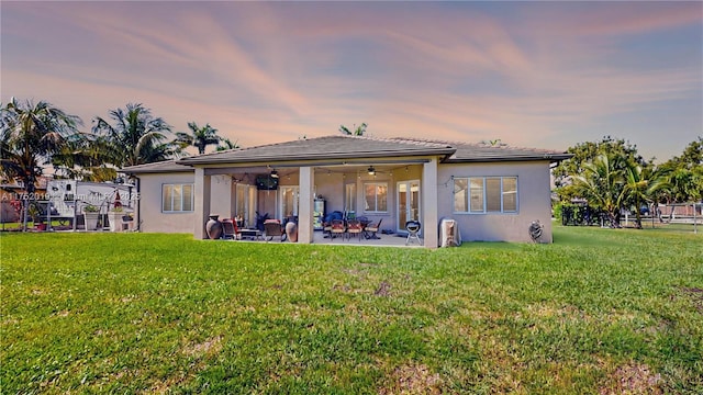 back of house with ceiling fan, a patio, a lawn, and stucco siding