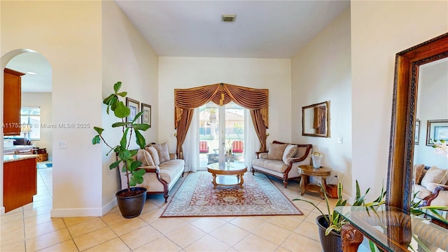 sitting room with arched walkways, a healthy amount of sunlight, baseboards, and light tile patterned floors