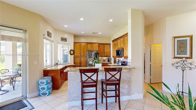 kitchen featuring light tile patterned floors, a peninsula, appliances with stainless steel finishes, light stone countertops, and brown cabinetry