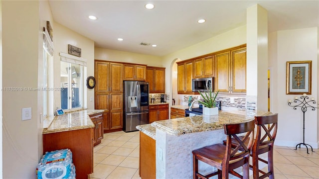 kitchen featuring a peninsula, light tile patterned floors, appliances with stainless steel finishes, and brown cabinets