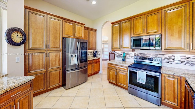 kitchen featuring appliances with stainless steel finishes, backsplash, light stone countertops, and brown cabinets