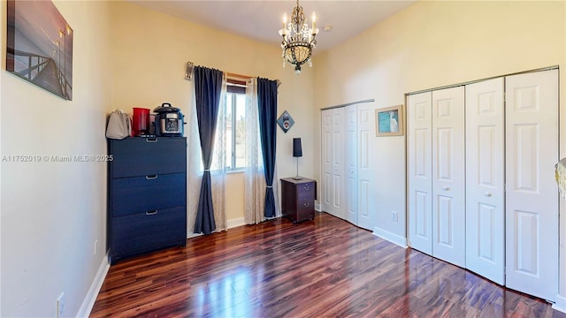 unfurnished bedroom featuring wood finished floors, an inviting chandelier, two closets, and baseboards