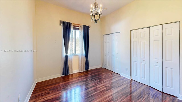 unfurnished bedroom with an inviting chandelier, wood finished floors, baseboards, and two closets